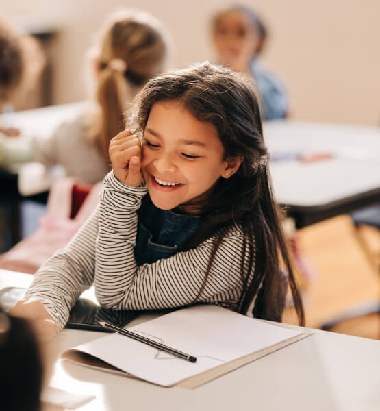 Young girl smiling while sitting at her desk in her classroom